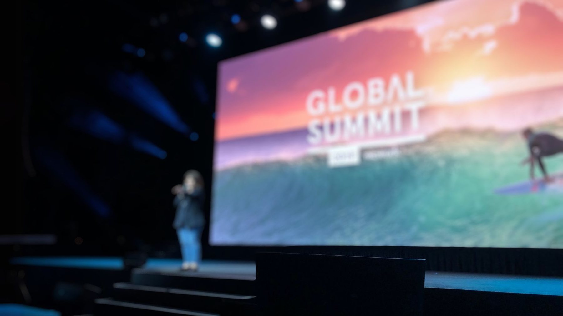 Ashley England on a conference stage in front of a large screen reading Global Summit